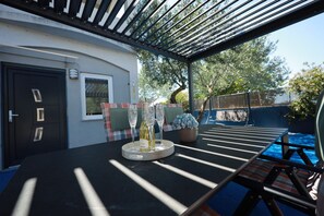 A covered outdoor seating area with a table, chairs, and a bottle of wine.