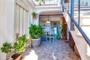 A sunlit courtyard with potted plants, a blue chair, and a staircase.