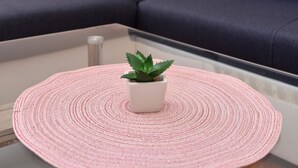 A modern living room with a dark grey sofa, a pink woven placemat, a small potted plant, a wall-mounted clock, and a wall sconce. - Studio apartment Eva- Old City Center (Zadar)