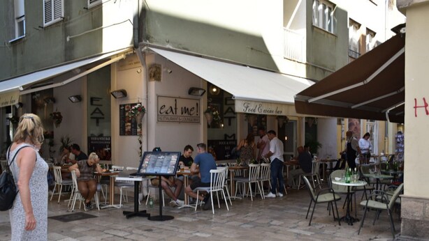 An outdoor café area with tables and chairs, a menu board, and a sign that reads "eat me!" - Studio apartment Eva- Old City Center (Zadar)