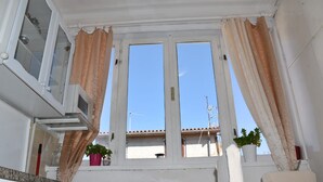 A room with a large window, white walls, a kitchen area with a stove, and a chair. - Studio apartment Eva- Old City Center (Zadar)