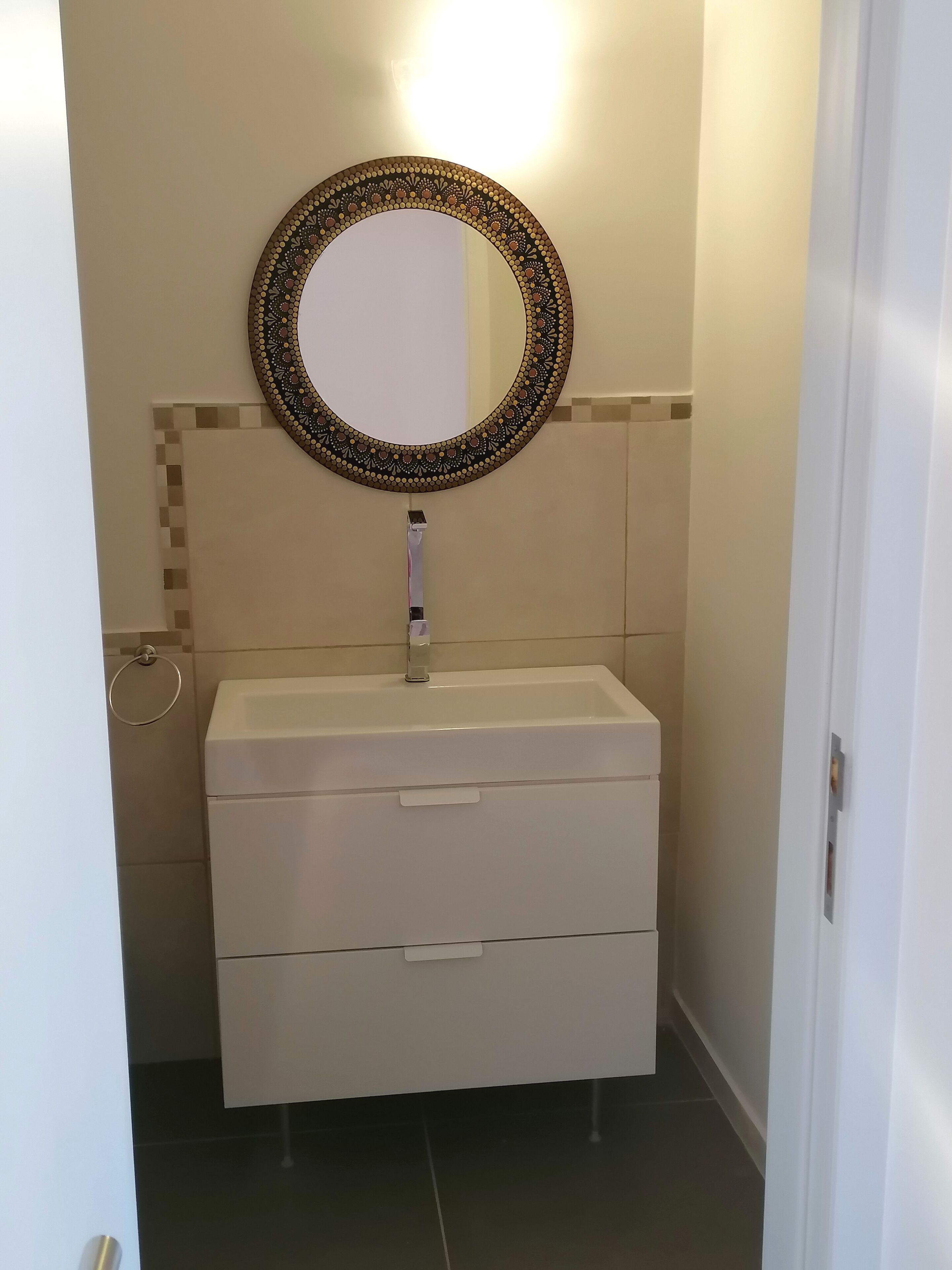 Een badkamer met een wit wastafelmeubel, een decoratieve spiegel en een handdoekhouder.