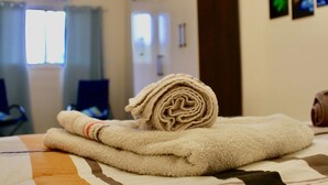 Una cama bien hecha con una toalla enrollada y una manta estampada.