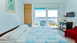 Quarto com cama, TV e varanda com vista para o mar.