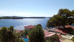 Uma propriedade costeira com telhados de telha vermelha, piscina e vista para o mar e colinas ao longe.