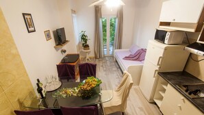Ein gemütlicher Raum mit Bett, Esstisch und Stühlen, einer kleinen Küchenzeile und Blick ins Freie durch eine Tür.