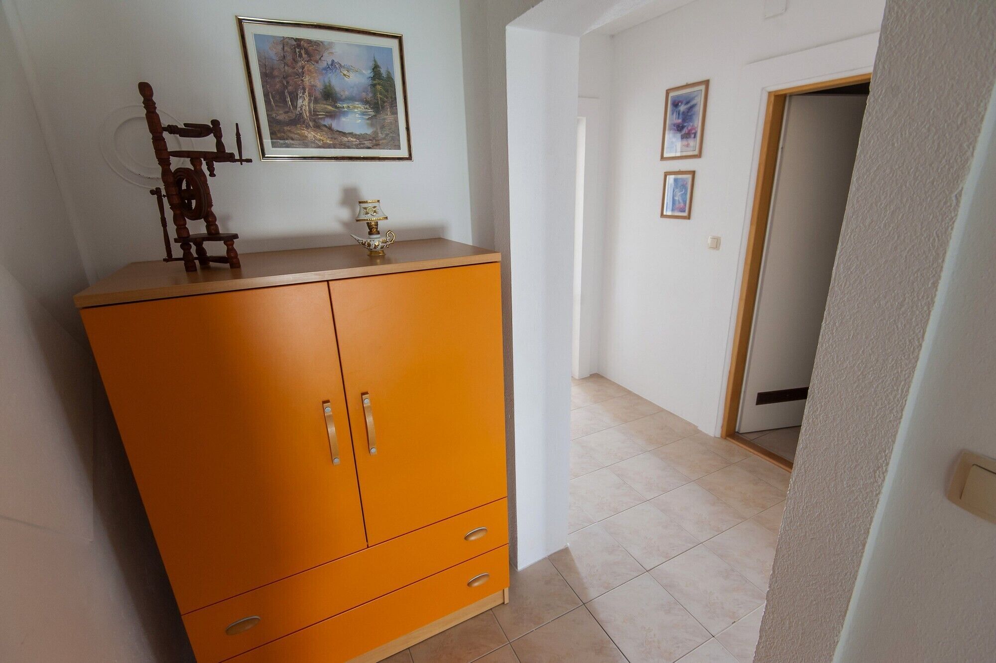Een gang met een houten kast, een schilderij en een deur naar een andere kamer.