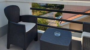 A balcony with wicker furniture, a clear view of neighboring buildings, and a tiled roof.