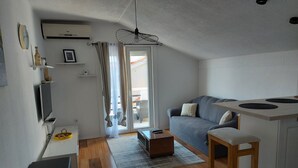 A compact living space with a kitchenette, a grey sofa, a wooden dining table, and a small kitchen counter.