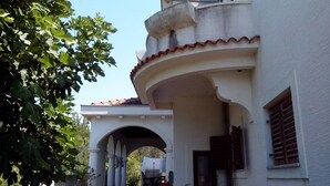 Un bâtiment à la façade blanche, doté d’un balcon incurvé et d’une arche menant à un patio abrité.
