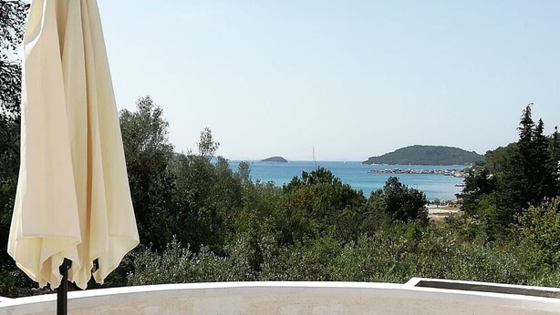 Une table avec un vase de fleurs et une tasse, placée devant un paysage pittoresque de la mer et des collines.