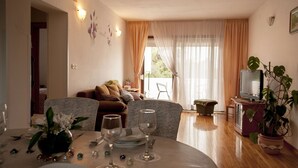 Un coin repas avec une table ronde dressée pour deux personnes, un canapé en arrière-plan et un téléviseur dans un coin.