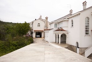 Un bâtiment blanc avec une allée menant à un garage. Des arbres et des arbustes se trouvent sur le côté gauche.