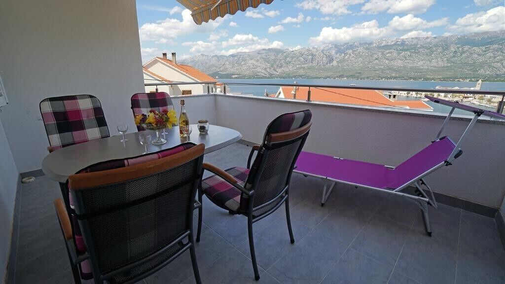 A balcony with a table and chairs, a purple cushioned bench, and a view of a lake and mountains.