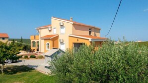 A two-story house with a tiled roof, a small garden, and a clear blue sky.