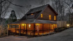 A log cabin with a porch, a staircase, and a small shed.