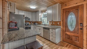A kitchen with granite countertops, white cabinetry, a wooden door with a glass panel, and a small island with a bench.