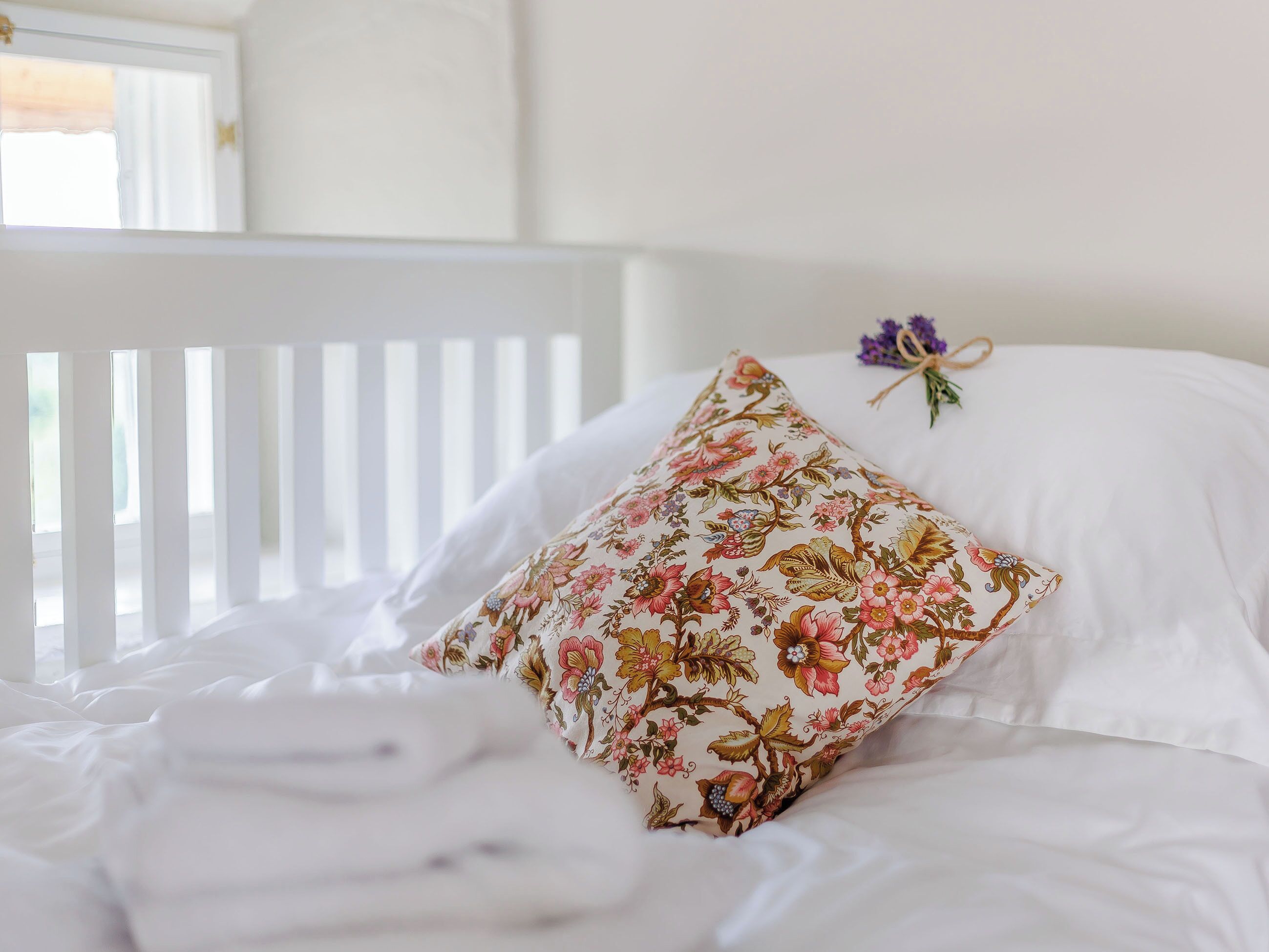A bed with white bedding and a floral pillow.