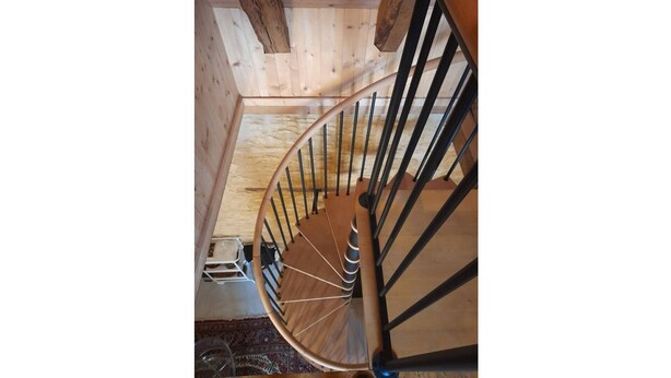 Una escalera en espiral de madera con barandillas de metal negro y pasamanos de madera.