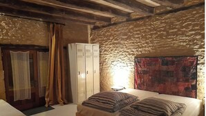 Un dormitorio con pared de piedra, cama con ropa de cama a rayas, armario y una pequeña mesa redonda.