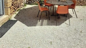 Un patio al aire libre con una pared de piedra, una mesa redonda de madera, cuatro sillas naranjas y un paraguas grande.