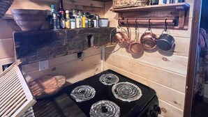 Une cuisine avec des étagères en bois où sont rangés divers ustensiles, une cuisinière à quatre brûleurs et un porte-casseroles fixé au mur.