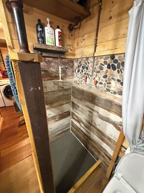 A small, rustic bathroom with wooden walls, a stone mosaic backsplash, and a shower area. - Darling cottage near entrance to Letchworth State Park  overlooking Silver Lake! (Castile)