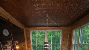 Une table à manger en bois, avec six chaises, un luminaire suspendu et une vue sur la verdure grâce à de grandes fenêtres.