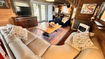 A cozy cabin interior with a sofa, a coffee table, a television, and a kitchen area.