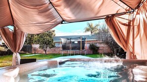 A hot tub with a digital control panel, surrounded by a covered area with beige curtains. - Beautiful and Cozy 4-BR residential home! (Oxnard)