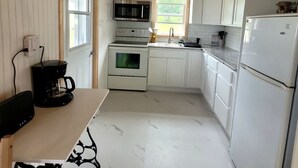A compact kitchen with white cabinetry, a microwave, an oven, a sink, and a refrigerator. - Quaint 2 bedroom water view cottage.  Near great golfing, beaches and breweries. (Lower Montague)