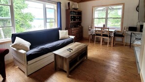 A cozy room with a wooden ceiling, a sofa, a dining table, and a bookshelf. - Quaint 2 bedroom water view cottage.  Near great golfing, beaches and breweries. (Lower Montague)