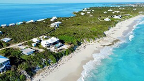 Vue aérienne d’une propriété située sur la côte, avec plusieurs bâtiments blancs, une plage de sable et une vue dégagée sur l’océan.