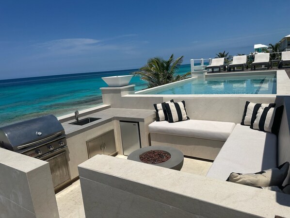 A modern outdoor seating area with a pool, grill, and ocean view.