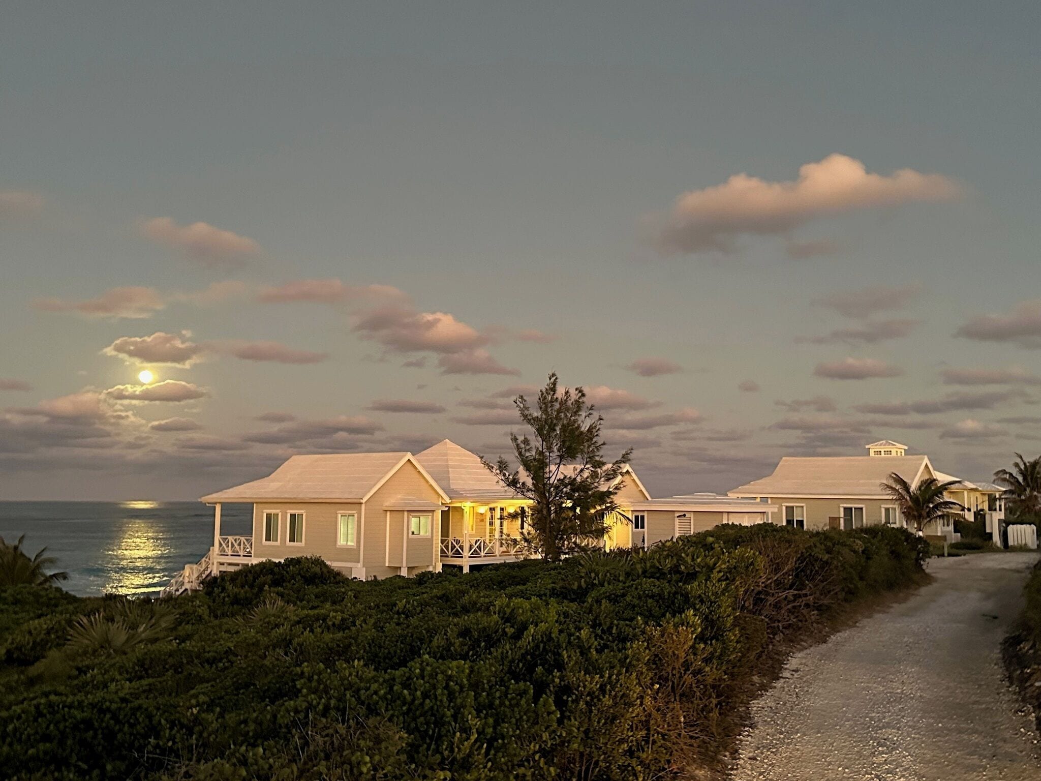 A coastal property with a paved driveway leading to a house with a balcony.