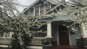 A two-story house with a porch, a visible number '590', and a tree with white blossoms in front.