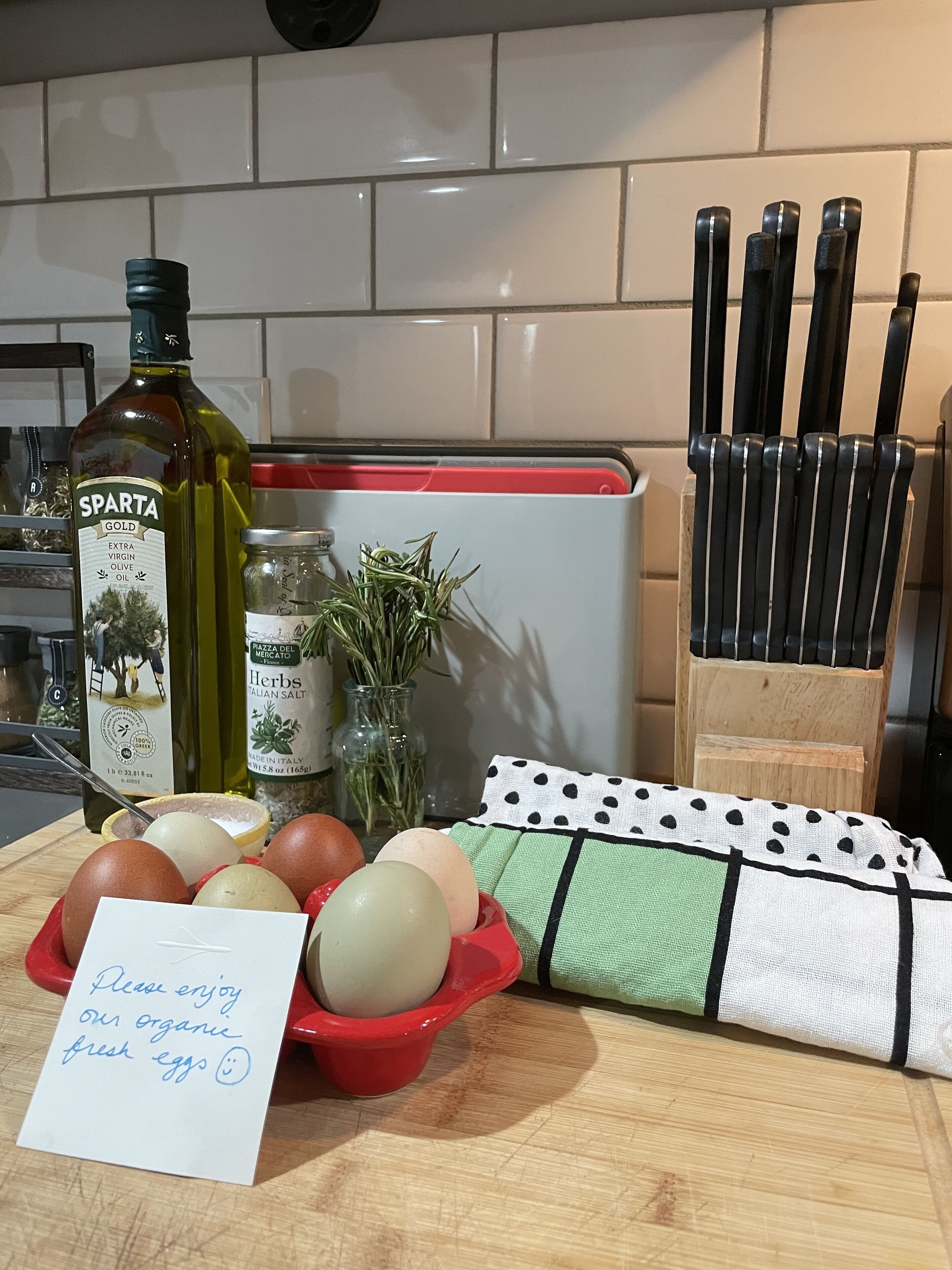 Un plan de travail de cuisine avec une bouteille d’huile d’olive, un pot de sel italien, un panier d’œufs et un mot.