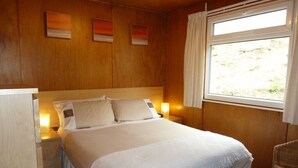 Et soveværelse med en stor seng, trævægge, et vindue med gardiner og et natbord med lampe.