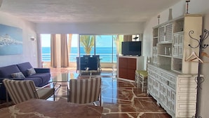 A spacious living room with a marble floor, a sofa, striped chairs, a TV, and a cabinet with decorative items.