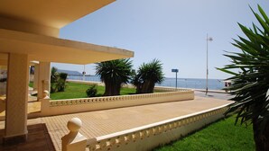 A covered outdoor area with a tiled floor, palm trees, and a view of the sea.