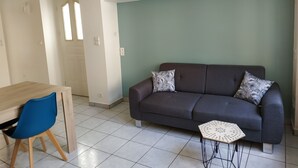 Un soggiorno con un divano grigio scuro, due cuscini decorati, un piccolo tavolino bianco e una poltrona blu.