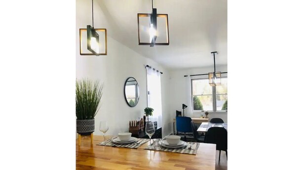 A modern dining area with a wooden table set for two, two pendant lights, a potted plant, and a mirror on the wall.