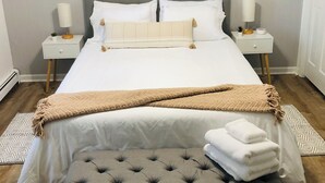 A neatly made bed with a grey headboard, two bedside tables with lamps, a bench, and a ceiling fan.