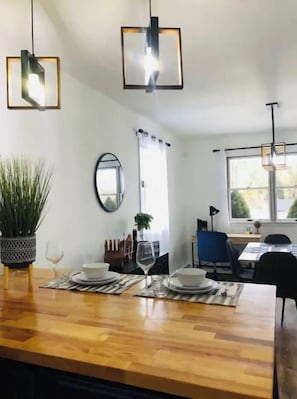 Ein moderner Essbereich mit einem Holztisch, gedeckt für zwei Personen, zwei Pendelleuchten, einem Topf mit Pflanze und einem Spiegel an der Wand.