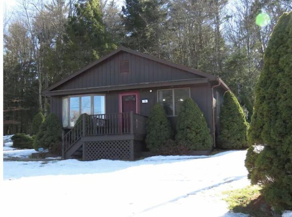 Cozy retreat nestled among evergreen trees, featuring a charming front porch and a warm red door.