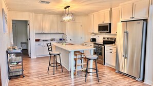 Cozinha moderna com armários brancos, eletrodomésticos de aço inoxidável, uma ilha central com banquetas e um candelabro.