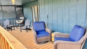 Uma área de estar coberta ao ar livre, com cadeiras de vime, uma mesa, piso de deck de madeira e parede azul.