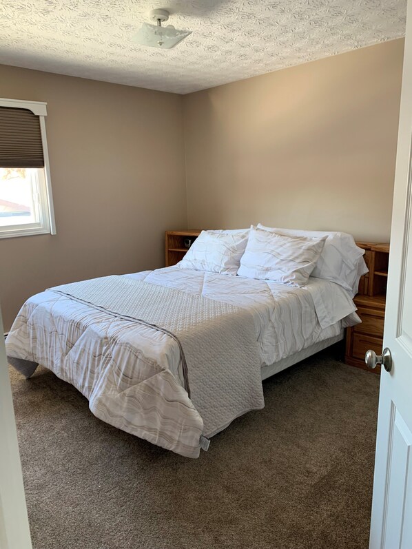 A bedroom with a bed, a nightstand, a ceiling fan, and a window with blinds.