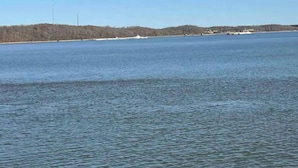 A wide view of a calm lake with a forested shoreline and a few buildings in the distance.