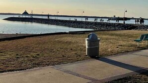 A waterfront park with a gazebo, a trash can, and a paved walkway.